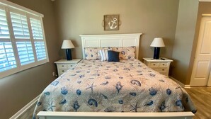 Un dormitorio con una cama, dos mesitas de noche, un reloj de pared y una ventana con persianas.