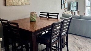 Un comedor con una mesa y sillas de madera, una lámpara decorativa y una cita inspiradora en la pared.