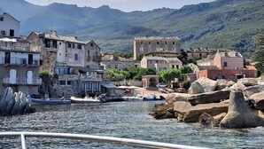 A coastal village with stone buildings, boats docked at the harbor, and mountains in the background.