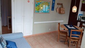 A living room with a blue sofa, a dining table with chairs, a kitchen area with a microwave, and a wall-mounted artwork.
