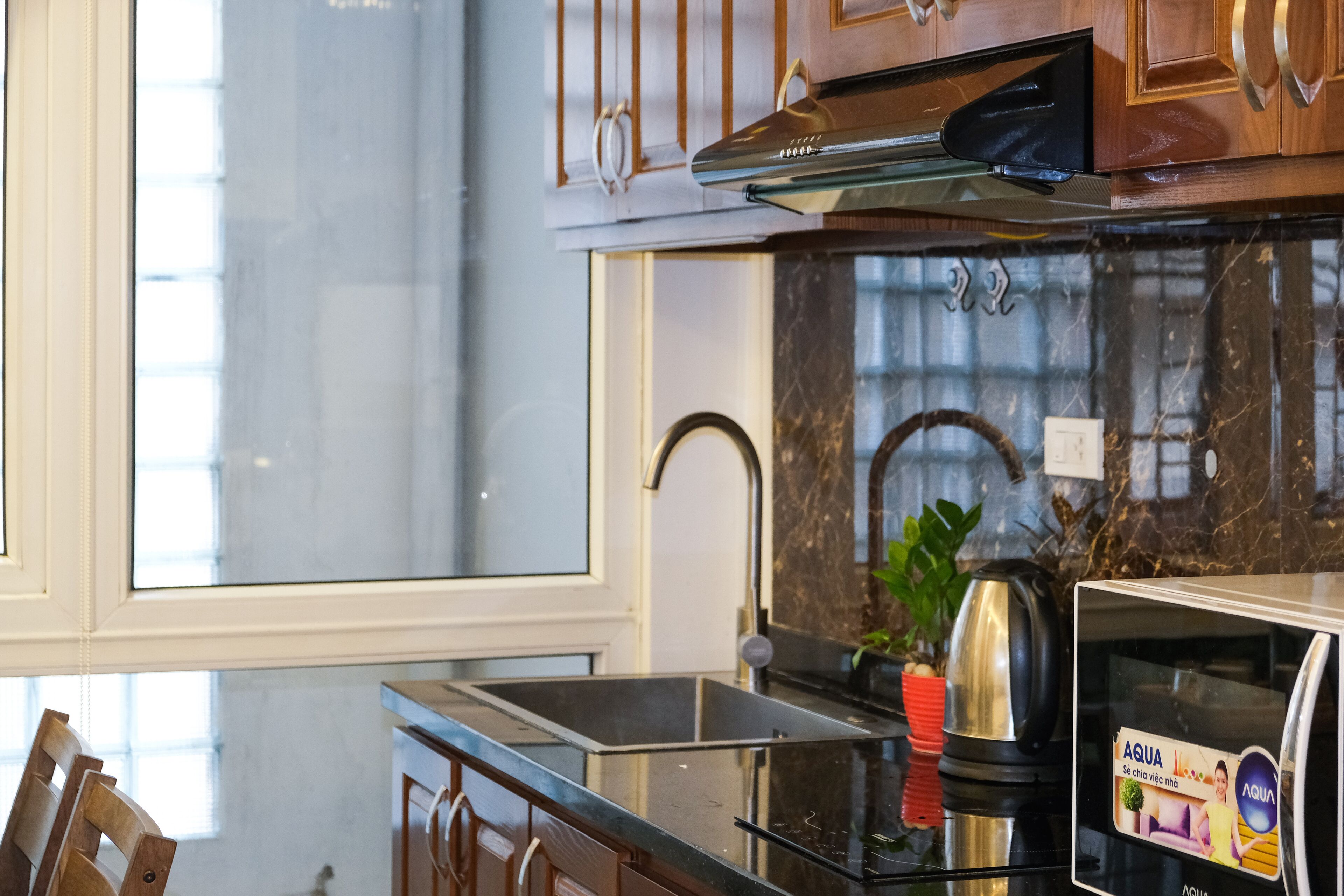 Una cocina con un lavamanos de acero inoxidable, armarios de madera y encimera de mármol.