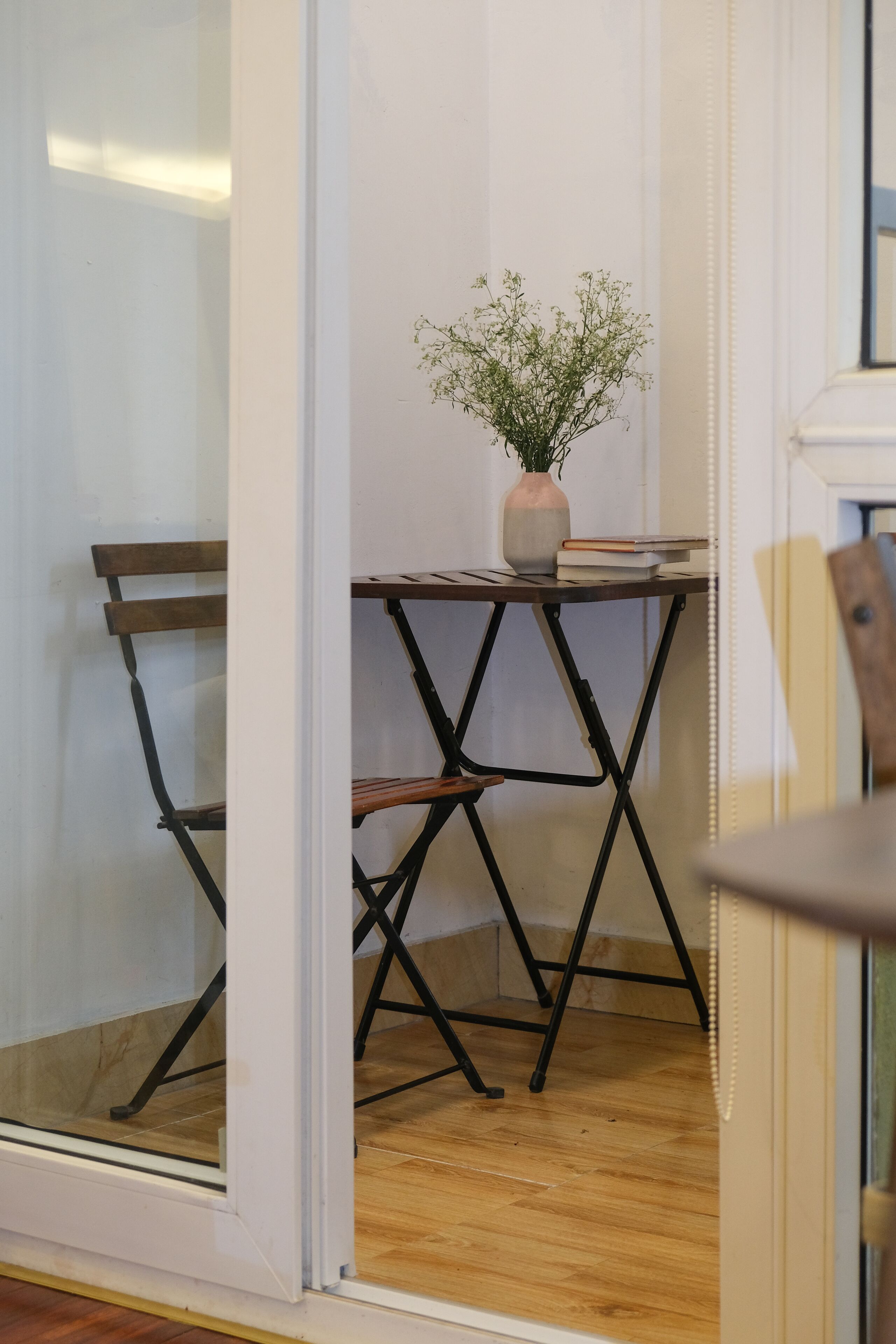 A room with a wooden floor, a small table with a vase of flowers, and a chair.
