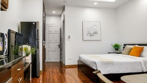 Habitació d'hotel moderna amb sòl de fusta, llit amb roba de llit blanca, taula petita i televisió sobre un moble de fusta.