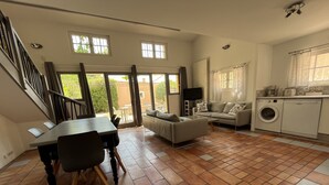 A spacious living area with a dining table, sofa, and a washing machine in the corner. - Shelby - Gîte Atypique 6 Personnes à 5mn D'uzès Style Loft Ambiance Automobile (Saint-Quentin-la-Poterie)