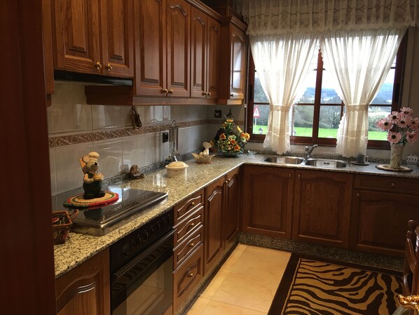 A kitchen with wooden cabinets, a granite countertop, a built-in oven, a sink, and a window with a view of the outdoors.