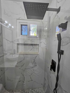 A modern bathroom with a shower, marble walls, and a small window. - Casa Margarita (Roatan)