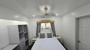 A bedroom with a bed, two bedside tables, a wardrobe, a ceiling fan, and a window with curtains. - Casa Margarita (Roatan)