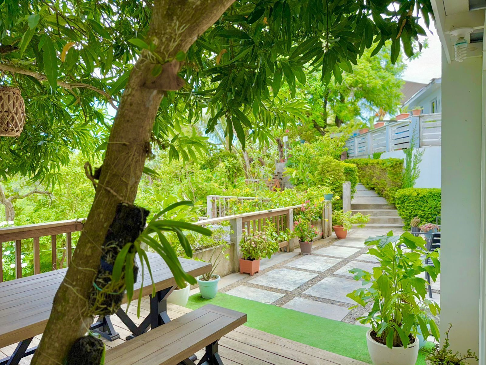 Eine Holzterrasse mit einer Bank, umgeben von Blumentöpfen und einer Treppe, die zu einem Haus führt.