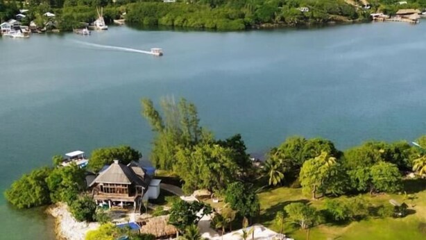 An aerial view of a coastal resort with a beach, clear waters, and lush greenery. - Casa Margarita (Roatan)