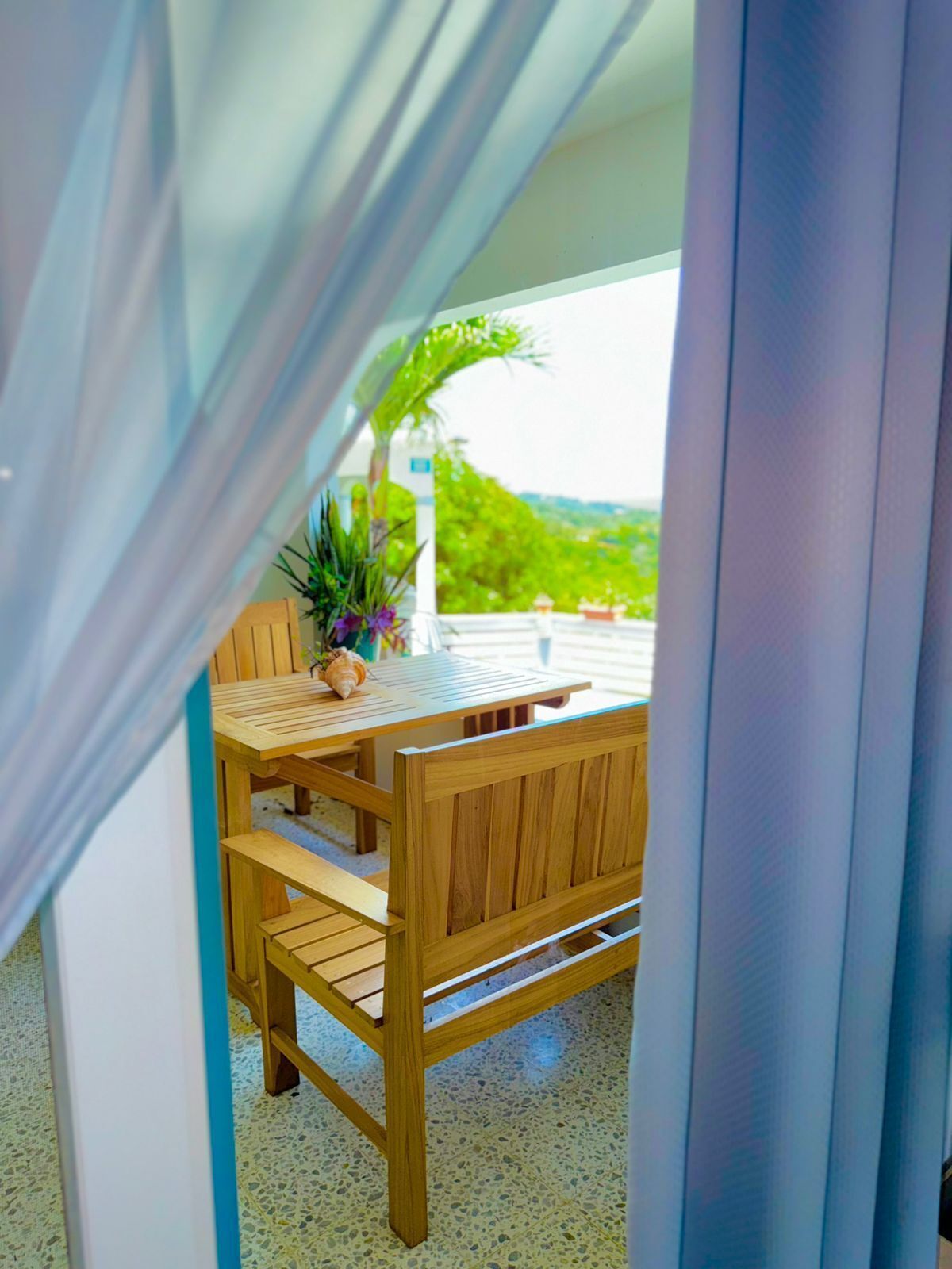 A wooden table and bench set on a balcony with a view of greenery.