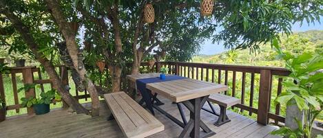 A wooden deck with a table and benches, surrounded by lush greenery and trees.