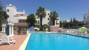 Une piscine entourée de bâtiments et de palmiers, avec des chaises longues et des parasols.