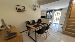 Un coin repas avec une table en bois, des chaises noires et une petite étagère où sont disposées des plantes en pot.