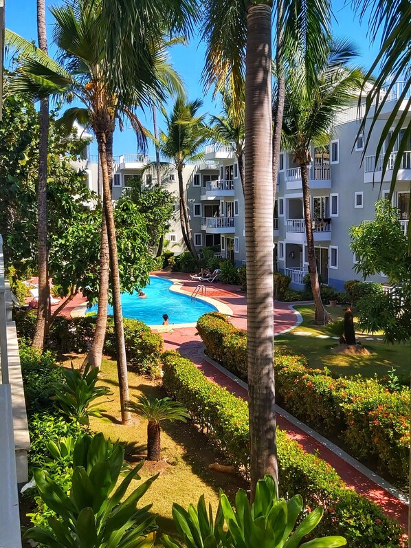 A pool area surrounded by palm trees and a multi-story building with balconies.