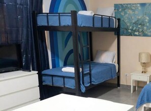 A bunk bed with a television on a white dresser, a small bedside table with a lamp, and a painting on the wall. - Sol Caribe Beach Group (Punta Cana)