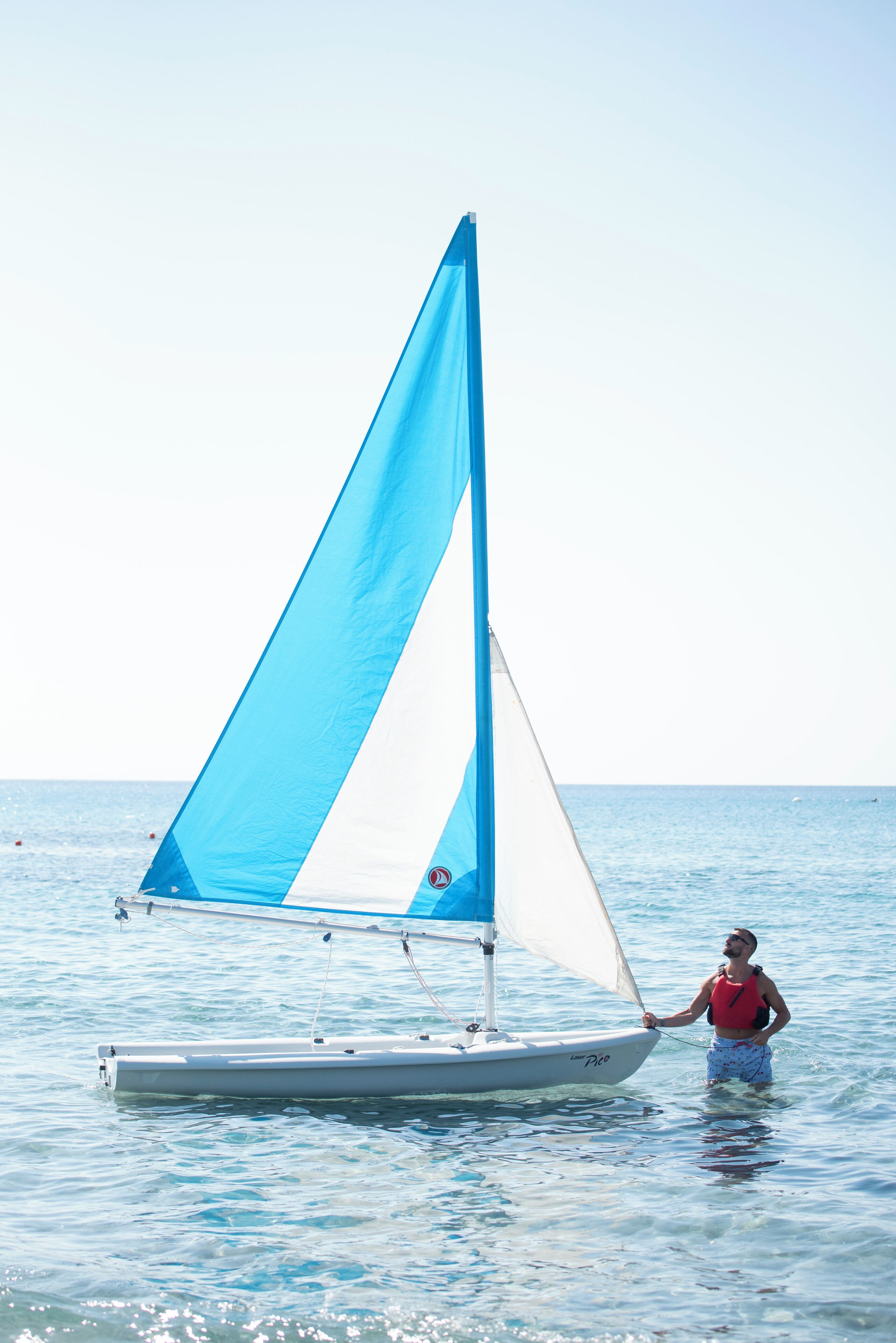 Una persona navegando en un pequeño bote con vela azul y blanca sobre aguas tranquilas.