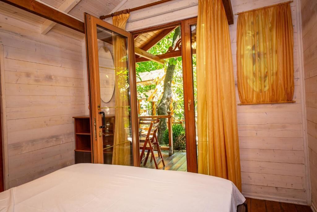 Una habitación de madera con una cama, una escalera de madera y vistas a un espacio exterior con terraza de madera y follaje.