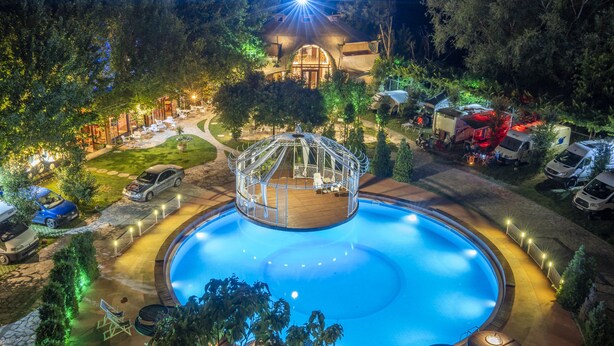 A swimming pool surrounded by a deck, with a gazebo in the center, and RVs parked nearby. - Hotel Legjenda (Shkodër)