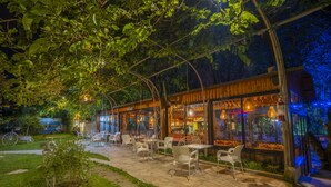 An outdoor café with tables and chairs under a wooden pergola, surrounded by greenery. - Hotel Legjenda (Shkodër)