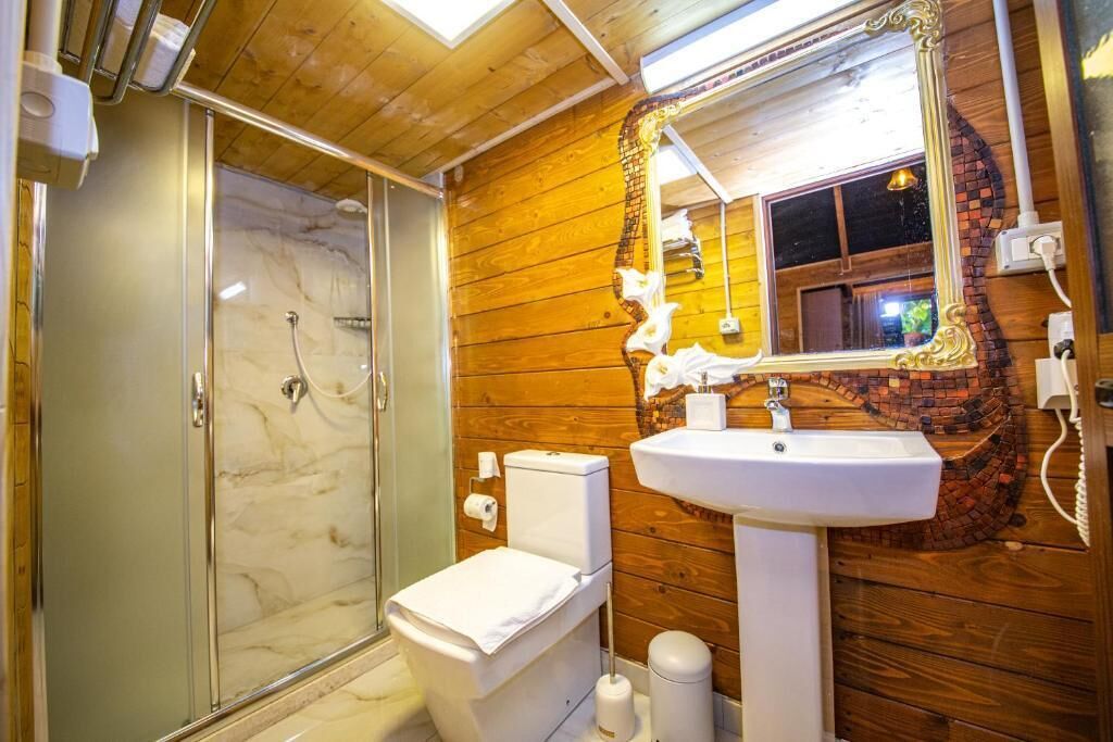 Un baño con cabina de ducha de vidrio, inodoro blanco, lavabo con espejo decorativo y paneles de madera en las paredes.