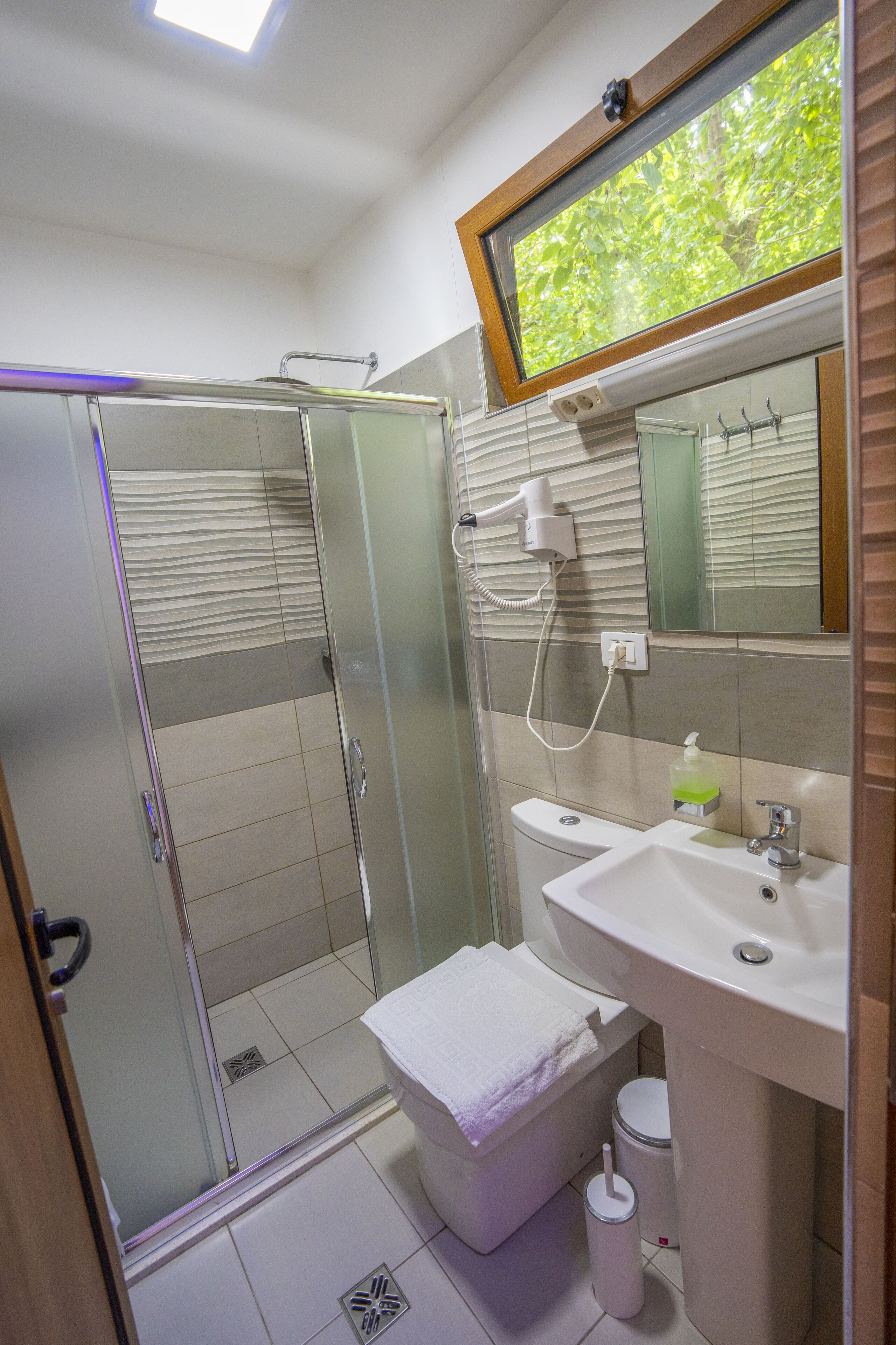 Un baño moderno con ducha envuelta en vidrio, lavamanos blanco y espejo sobre él.
