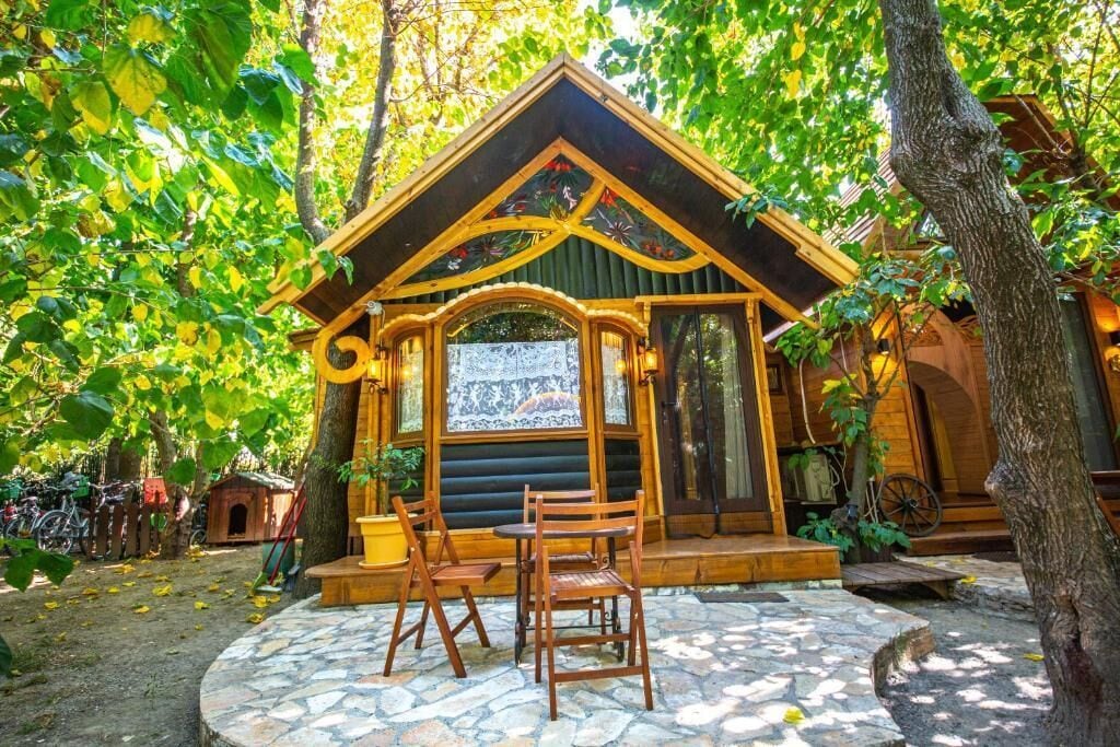 Una cabaña de madera rústica con un patio de piedra, sillas de madera y una bicicleta.