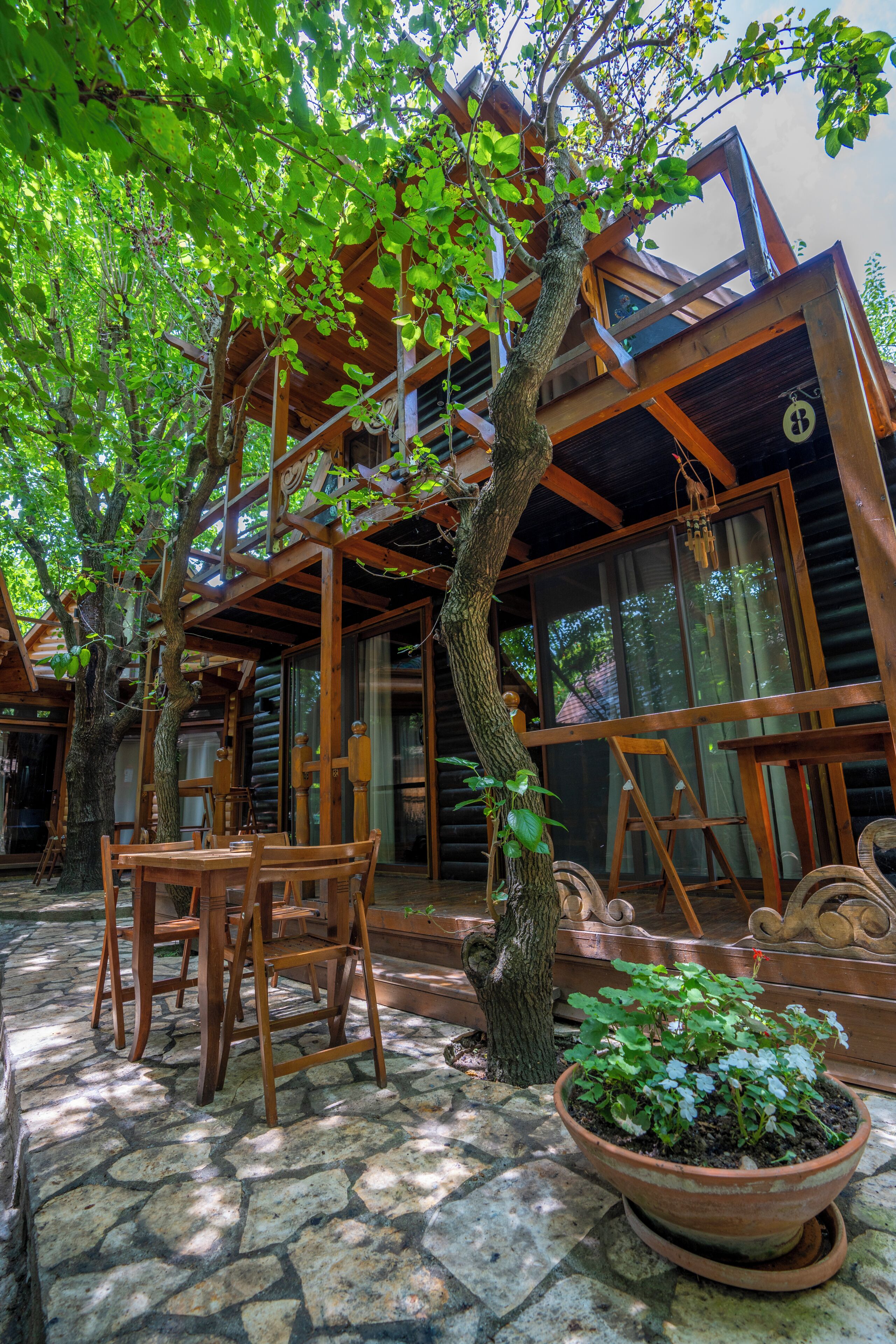 Une cabane en bois avec un patio en pierre, des meubles en bois et une grande plante en pot.