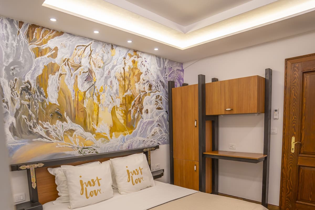 Un dormitorio con cama, un armario de madera, una pared con un cuadro e iluminación empotrada en el techo.