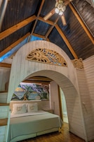 Une chambre avec un plafond en bois, un lit recouvert de linge de lit blanc et un arc décoratif en bois.