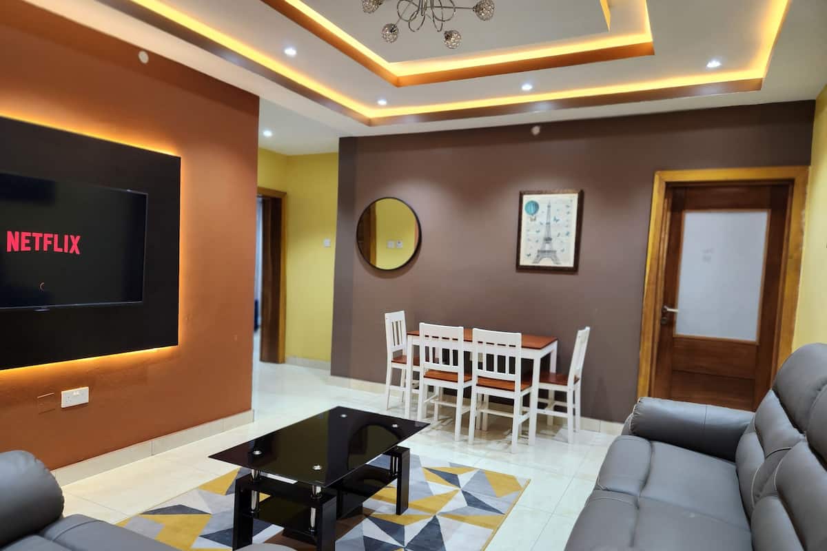 A modern living room with a flat-screen TV, a coffee table, sofas, a dining table with chairs, and a wall-mounted mirror.