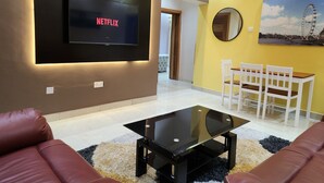 Ein modernes Wohnzimmer mit einem flachbildfernseher an der Wand, einem Glastisch, einer Couch, einem Esstisch mit Stühlen und einem Bild von einem Riesenrad.