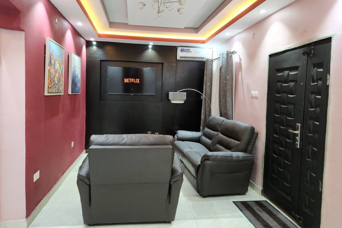 A modern living room with a sofa, a recliner, a TV mounted on the wall, and a black door.
