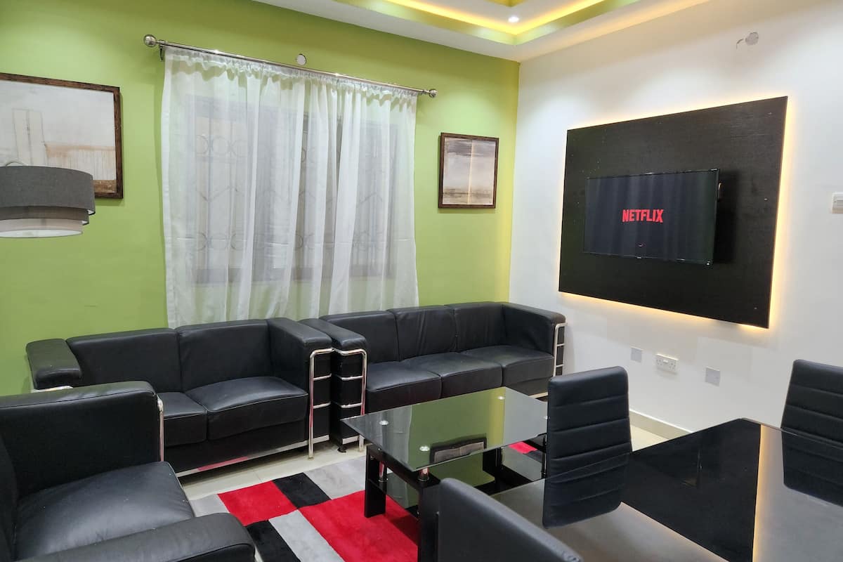 A modern living room with a sectional sofa, a glass coffee table, and a flat-screen TV mounted on the wall.