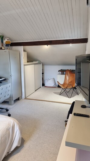 A compact room with a bed, a desk, a chair, a television, and storage cabinets.
