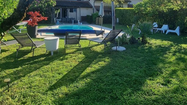 Una casa con piscina, rodeada por un césped cuidado y árboles.