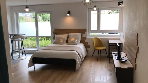 A bedroom with a bed, a desk, a chair, and two windows. - Studio 35 m2 Refait à Neuf (Fougères)