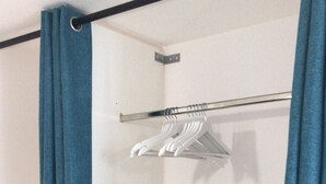 A walk-in closet with a metal rod for hanging clothes, a white shelf unit, and blue curtains. - Studio 35 m2 Refait à Neuf (Fougères)