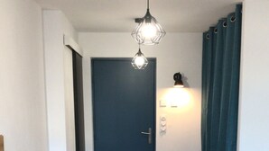 A hallway with a wooden floor, a blue door, a black TV stand, and a pendant light. - Studio 35 m2 Refait à Neuf (Fougères)