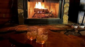 A stone fireplace with a fire, two glasses of beer on a wooden table, and a television on the right.