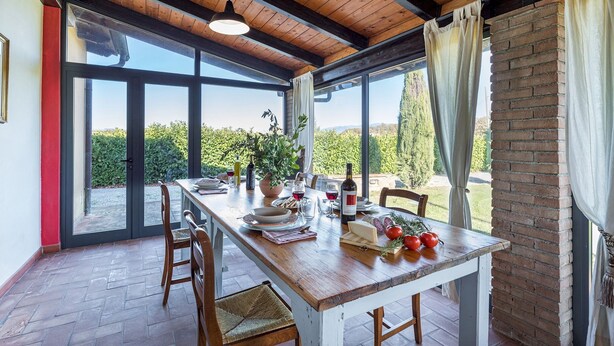 A dining area with a wooden table set for two, a potted plant, and a bottle of wine. - La Vigna 4, Emma Villas (Pogi)