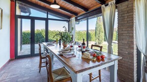Un coin repas avec une table en bois dressée pour deux personnes, une plante en pot et une bouteille de vin.