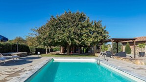 A swimming pool with a pergola and lounge chairs, surrounded by trees and a stone wall. - La Vigna 4, Emma Villas (Pogi)