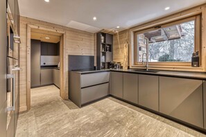 A modern kitchen with wooden accents, built-in appliances, and a large window.