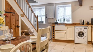 Une cuisine avec un escalier en bois, un lave-linge et un coin repas comprenant des chaises et une table.