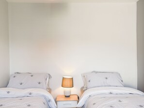 A bedroom with two beds, each with striped bedding and bee patterns, a nightstand with a lamp, and a small drawer.
