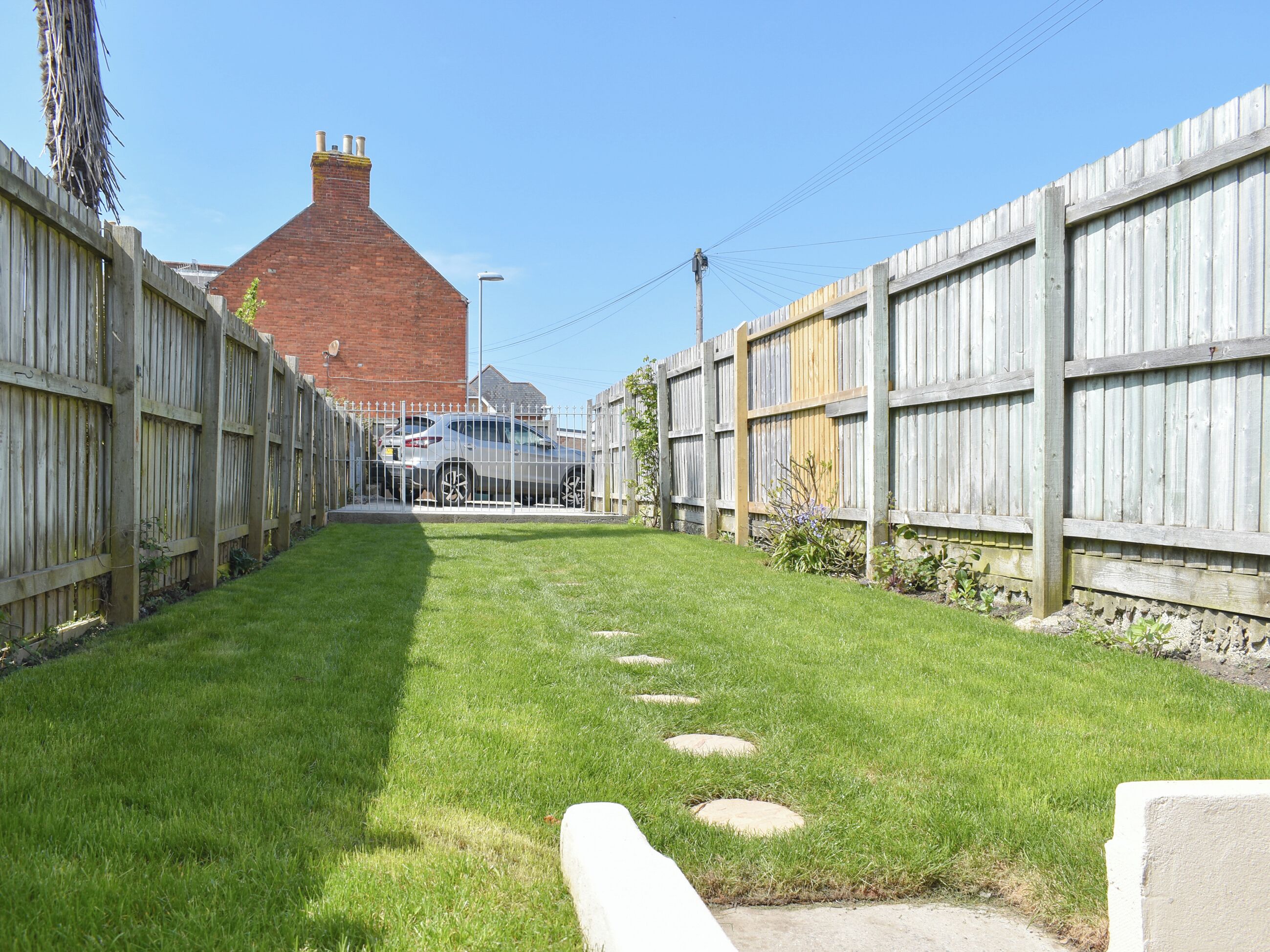 A narrow, grassy pathway flanked by wooden fences leading to a parked car.