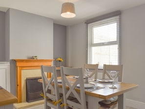 Uma sala de jantar com mesa de madeira, cadeiras brancas e lareira.
