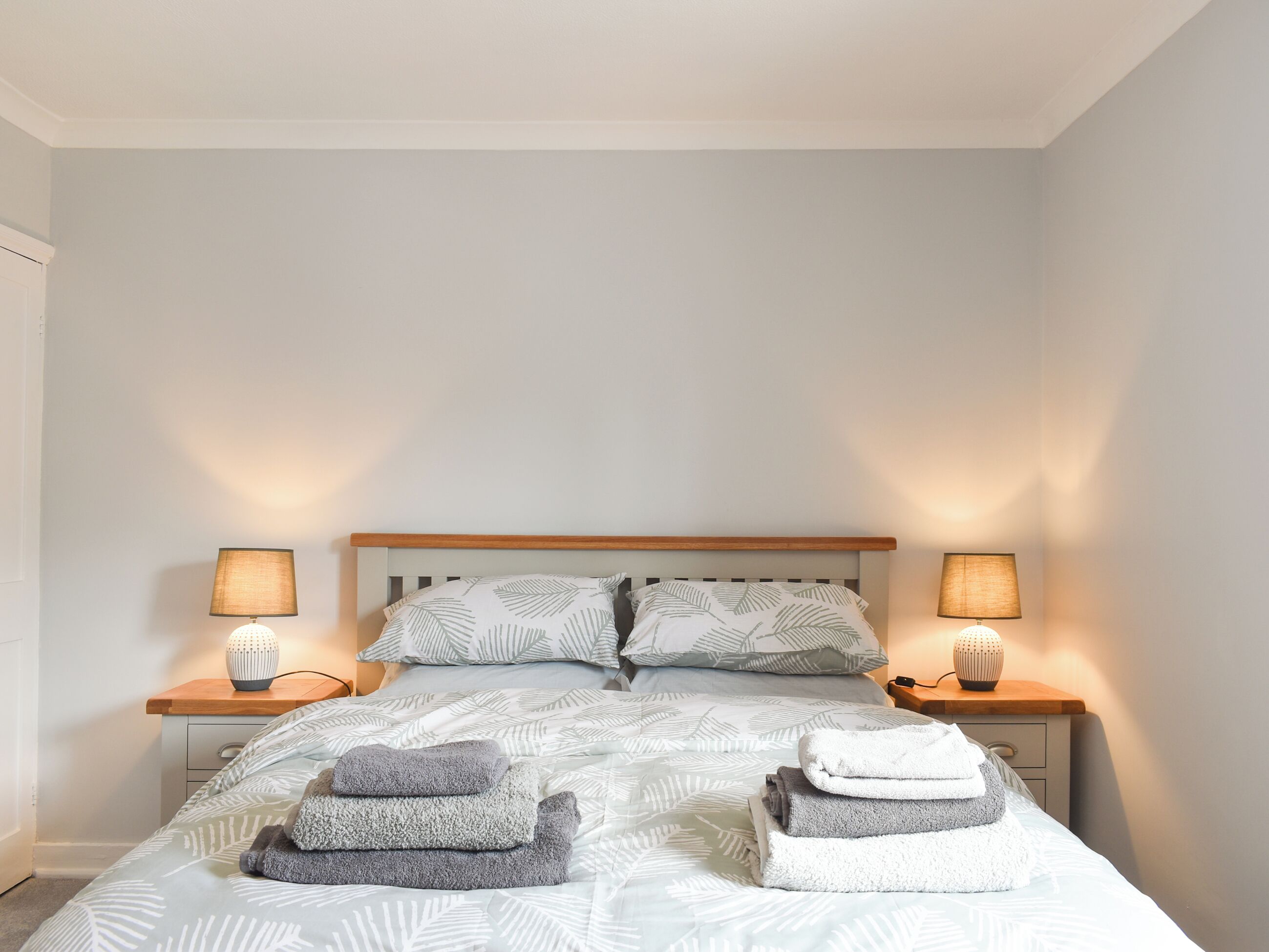 Un lit bien fait, avec une couette à motifs de feuilles, deux lampes de chevet et des serviettes pliées posées sur le lit.