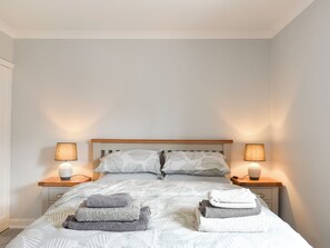 Un lit bien fait, avec une couette à motifs de feuilles, deux lampes de chevet et des serviettes pliées posées sur le lit.