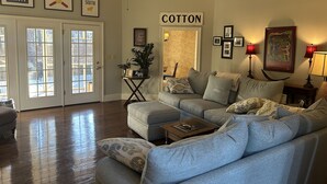 Ein Wohnzimmer mit einem Ecksofa, einem Deckenventilator und einer Tür mit der Aufschrift 'COTTON'.